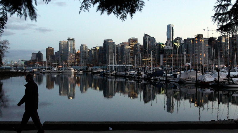A man walks in Stanley Park as the skyline of Vancouver is reflected in water in Vancouver, Friday, Feb. 5, 2010. (AP / Jae C. Hong)
