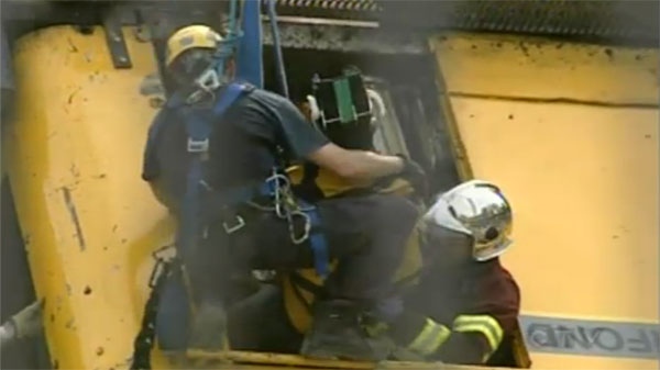 An emergency worker hanging in a harness removes the crane operator - with her head secured - from the cabin.