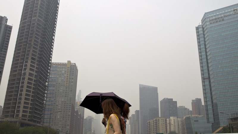 Chinese women holding an umbrella shield themselves from the sun as they walk past the hazy Beijing skyline on Monday, June 20, 2011. (AP Photo/Andy Wong)