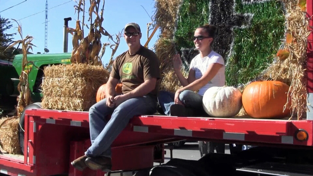 Two people on a tractor posing with pumpkins