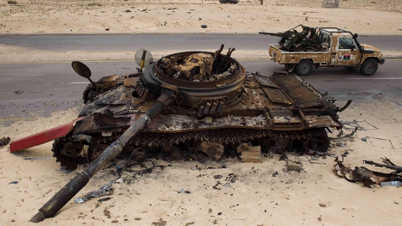 In this April 20, 2011 file photo, Libyan rebel fighters drive by a previously-destroyed pro-Gadhafi forces tank on the outskirts of Ajdabiya, Libya. (AP Photo/Bernat Armangue)