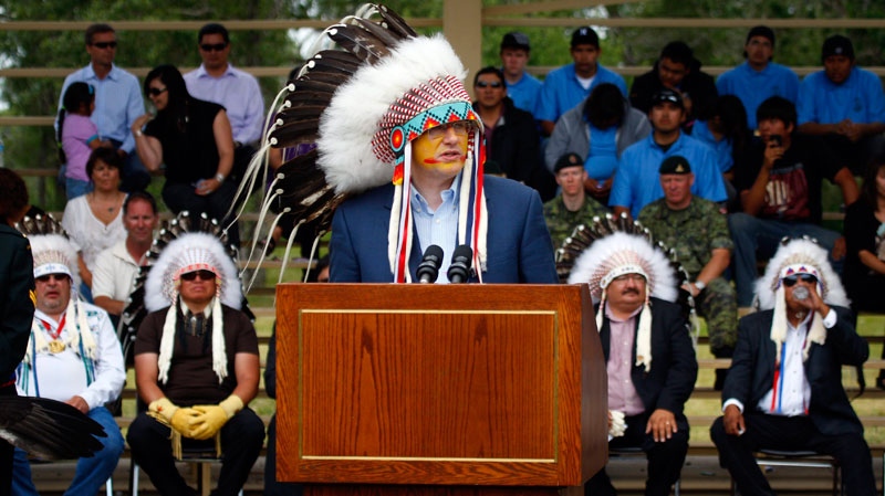 Prime Minister Stephen Harper, centre, delivers a speech wearing a headdress after being made an honorary chief of the Blood tribe during a ceremony in Stand Off, Alta., Monday, July 11, 2011. (Jeff McIntosh / THE CANADIAN PRESS)