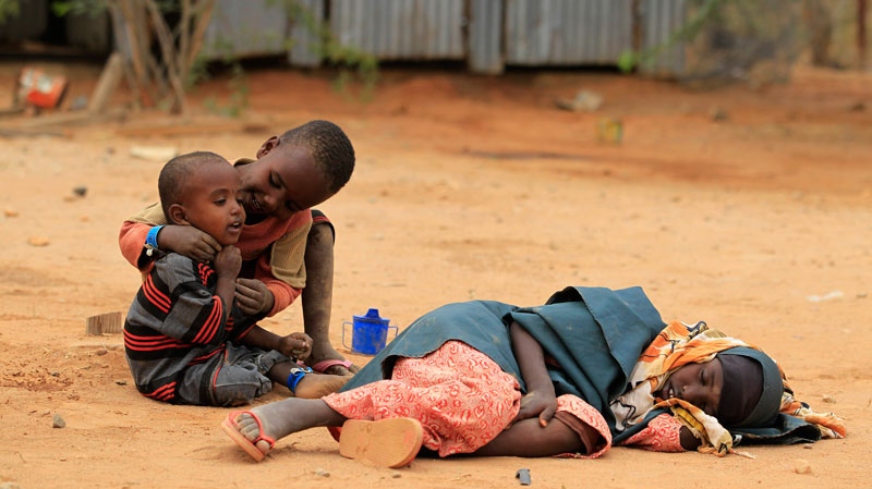 A Somali girl sleeps on the ground as other children play while waiting to register as refugees, in Ifo Camp, outside Dadaab, Kenya, Thursday, July 14, 2011. (AP/ Rebecca Blackwell)