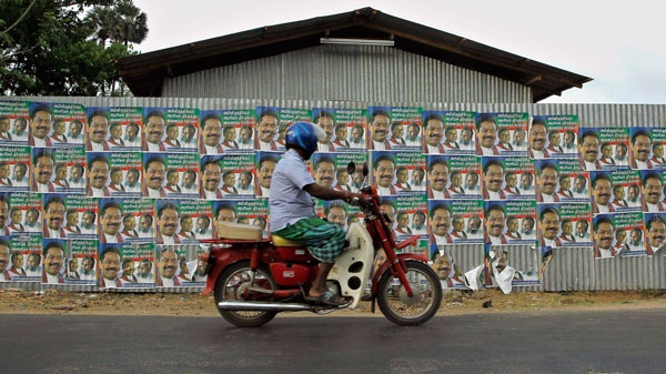 An ethnic Sri Lankan Tamil rides a scooter against a wall pasted with election propaganda of Sri Lankan President Mahinda Rajapaksa's ruling party, in Jaffna, Sri Lanka, Friday, July 22, 2011. (AP / Eranga Jayawardena)