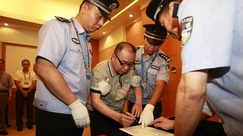 In this photo released by China's Xinhua news agency, Lai Changxing, center, signs a warrant issued for his arrest as he arrives at the Beijing Capital International Airport in Beijing, on Saturday July 23, 2011. (AP / Xinhua,Zhang Jianxin) 