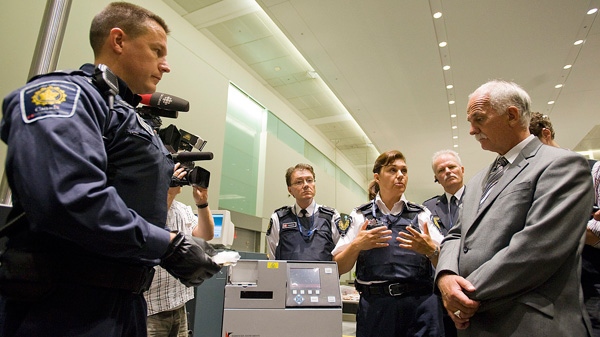 Public Safety Minister Vic Toews, right, watches as CBSA officer John Shortill, left, and Rhonda Rabi, chief of operations for terminal one, demonstrate the IONSCAN machine used to detect drugs during a demonstration of a typical secondary examination involving travellers arriving from abroad by the Canadian Boarder Services Agency at Pearson Airport in Toronto on Tuesday, August 9, 2011. (Aaron Vincent Elkaim / THE CANADIAN PRESS)