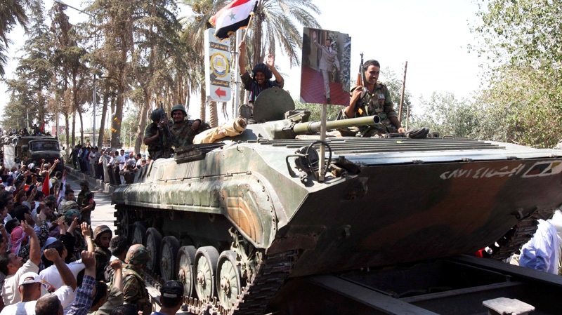 In this photo taken on a government-organized tour, Syrian soldiers salute residents as they sit atop their armored personnel carrier on their way out of the eastern city of Deir el-Zour, Syria, Tuesday, Aug. 16, 2011. (AP / Bassem Tellawi)