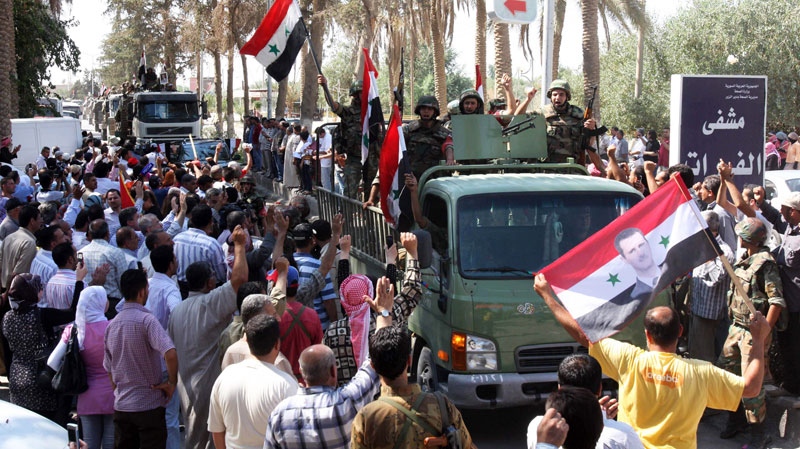 In this photo taken on a government-organized tour, Syrian soldiers atop military vehicles wave to residents on their way out of the eastern city of Deir el-Zour, Syria, Tuesday, Aug. 16, 2011. (AP / Bassem Tellawi)