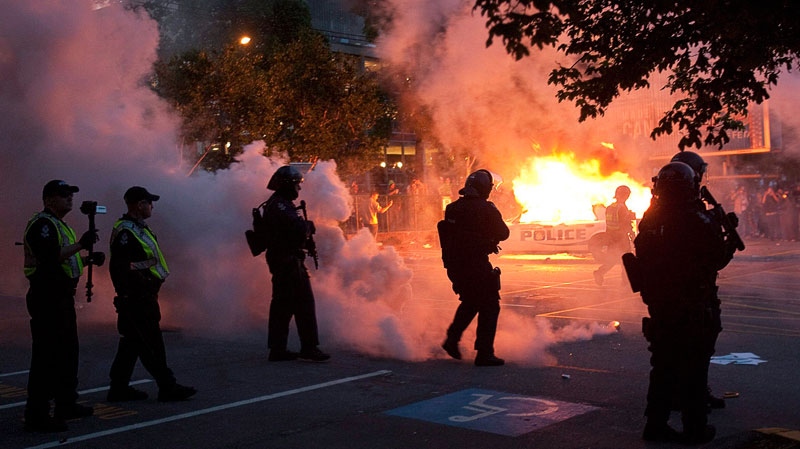 Riot police look on as two police cars burn during a riot in downtown Vancouver, Wednesday, June 15, 2011 following the Vancouver Canucks 4-0 loss to the Boston Bruins in game 7 of the Stanley Cup hockey final. Geoff Howe / THE CANADIAN PRESS