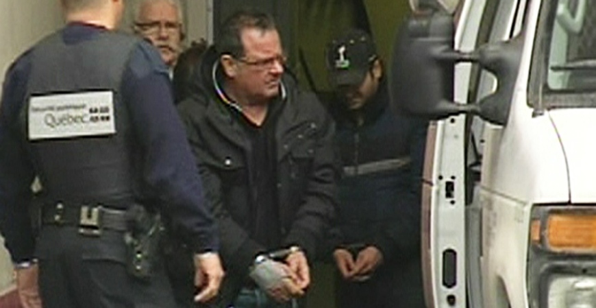 Raynald Desjardins, in handcuffs, exits a police v