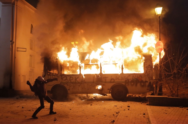 A protester throws a stone towards a burning police bus in front of him, during clashes with police, in central Kyiv, Ukraine, Sunday, Jan. 19, 2014. (AP / Efrem Lukatsky)