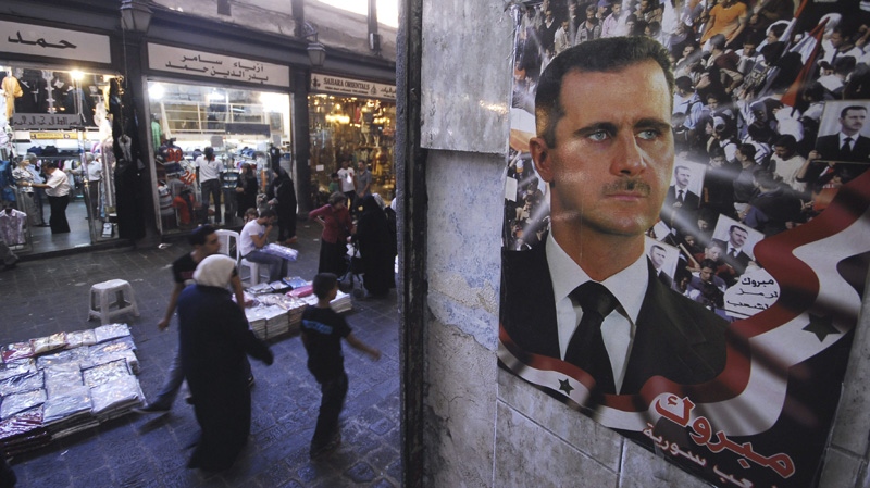 Syrian shoppers walk next to a portrait of Syrian President Bashar Assad with Arabic words read:"Congratulation for Syrian people," at the popular market of Hamidiyeh, in the old city of Damascus, Syria, on Saturday Sept. 3, 2011. (AP Photo/Muzaffar Salman)