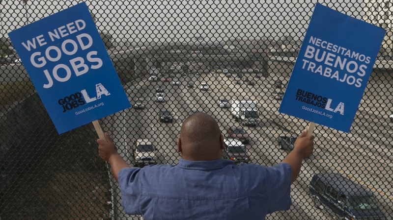 South Los Angeles resident Christian Del Cid waves banners calling for good jobs, on a bridge in front of oncoming traffic at the Interstate I-110 overpass on a "structurally deficient" bridge to call on U.S. Congress to provide funding for highway improvement projects that would create local jobs Thursday, Sept. 22, 2011, in Los Angeles. (AP Photo/Damian Dovarganes)