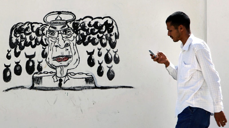 A Libyan man walks by a mural depicting Moammar Gadhafi in Tripoli