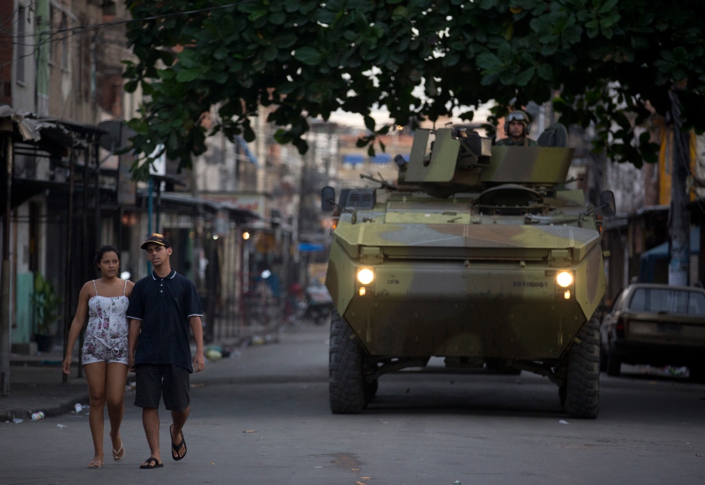 A couple walk pass a Navy armored in a Rio slum