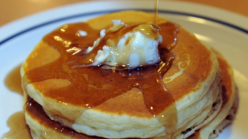 Maple syrup runs over a short stack of pancakes