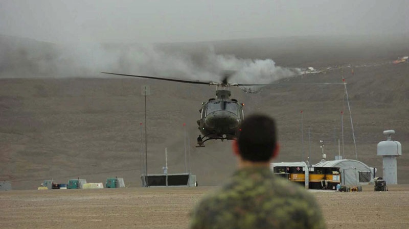 A member of the Canadian Forces watches a helicopter in front of a plane that crashed in the hills behind in Resolute Bay, Nunavut, Saturday, Aug.20, 2011. (The Canadian Press)