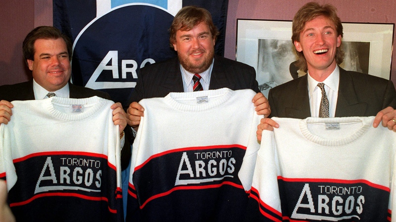 Los Angeles Kings owner Bruce McNall (left to right), comedian John Candy and hockey superstar Wayne Gretzky show off their new Argonaut jerseys in Toronto Feb. 25, 1991 after it was announced they purchased the CFL team. (Blaise Edwards / THE CANADIAN PRESS)