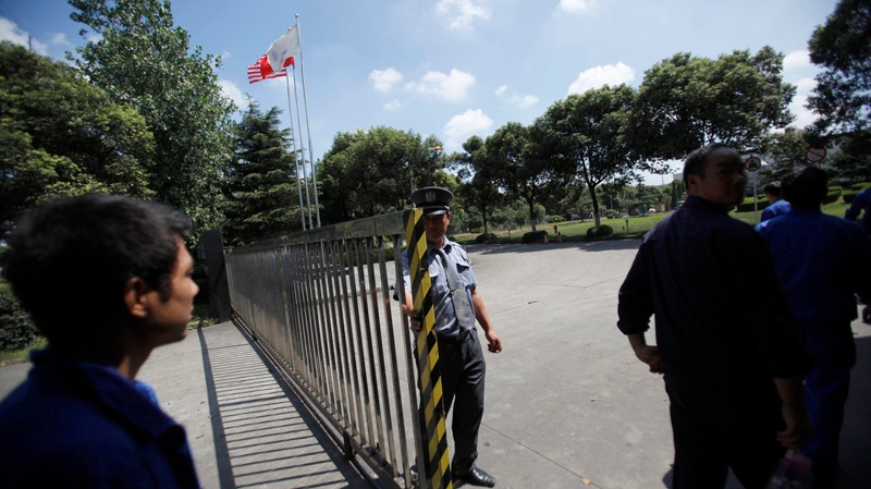 This Sept. 15, 2011 file photo shows a security guard closing the gate as workers walk in a battery factory of Johnson Controls nearby Kanghua New Village, in Shanghai, China. The U.S. battery maker said independent tests show that its factory in Shanghai was not the cause of severe lead poisoning cases discovered earlier this year but point instead to a nearby recycling facility.