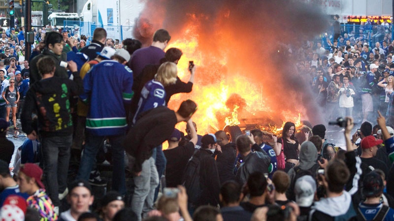 Stanley Cup rioters are seen next to a burning car in Vancouver on June 15, 2011. (Geoff Howe / THE CANADIAN PRESS)