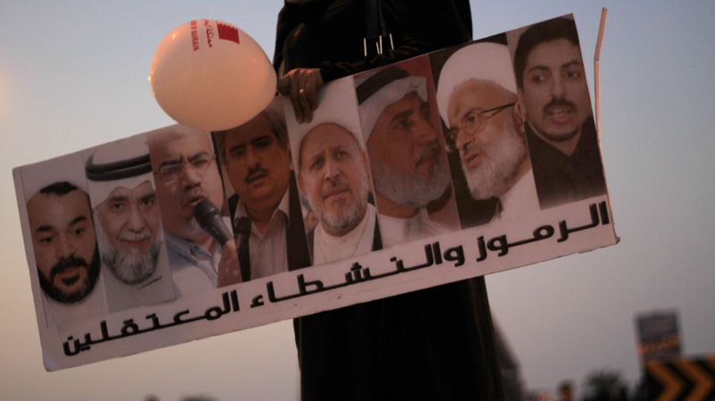 A Bahraini anti-government protester holds a banner with jailed opposition leaders' images, demanding their freedom Friday Dec. 30, 2011, during a protest near Abu Saiba, Bahrain, along a highway that runs past several Shiite Muslim villages. (AP Photo/Hasan Jamali)