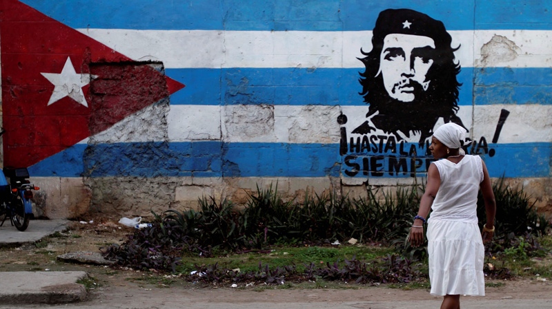 A santera looks back while crossing the street where a wall is covered with a mural of the Cuban flag and an image of Cuba's revolutionary hero Ernesto "Che" Guevara in Havana, Cuba, Friday Jan. 27, 2012. (AP Photo/Franklin Reyes)