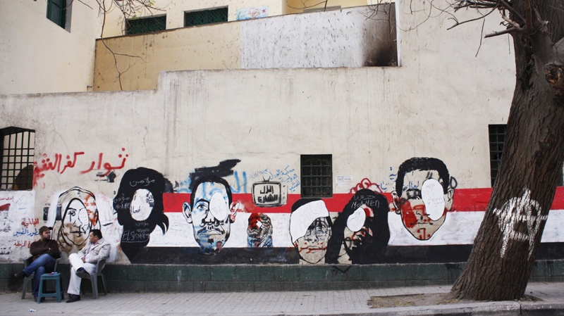 In this Saturday, Dec. 24, 2011 photo, men sit near revolutionary murals depicting those who lost their eyes during clashes near Tahrir Square in Cairo, Egypt.