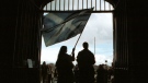 Two unidentified Scottish Nationalists stand at the entrance gate of the Scottish Parliament in Edinburgh, Scotland, wearing traditional dress and holding a Saltire flag and a broadsword, May 12, 1999. (AP / Louisa Buller, File)