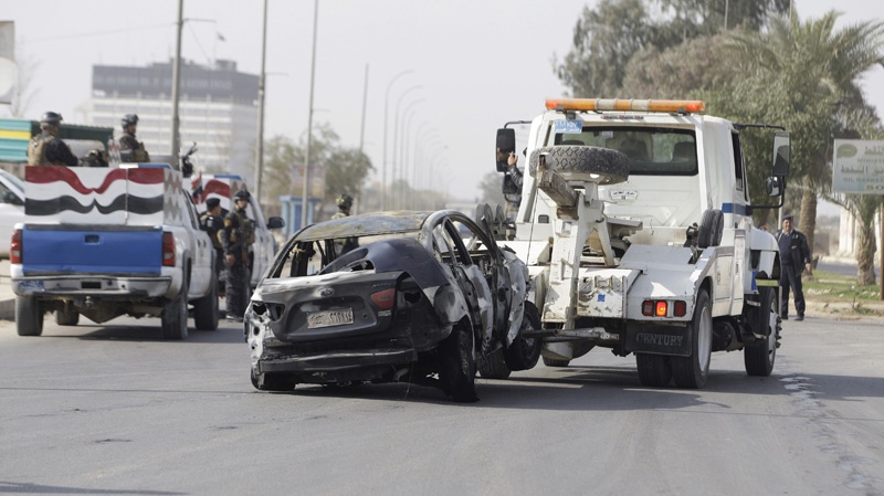 Security forces tow away a destroyed car after a car bomb attack outside the fortified academy near the Interior Ministry headquarters in Baghdad, Iraq, Sunday, Feb. 19, 2012. (AP Photo/Karim Kadim)