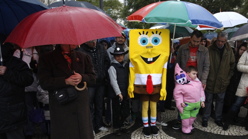 A child dressed as cartoon character SpongeBob joins others sheltering from the rain under umbrellas while watching a carnival parade Tuesday, Feb. 16 2010, in Lisbon.