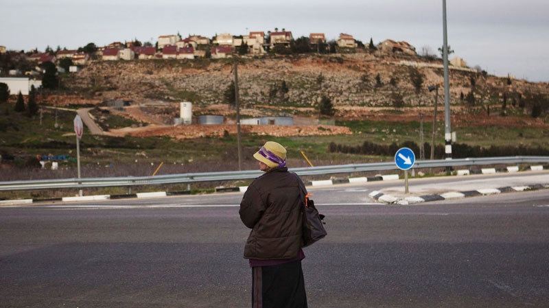 A Jewish settler woman waits for a ride outside the Jewish West Bank settlement of Shilo, background, Wednesday, Feb. 22, 2012. (AP / Bernat Armangue)