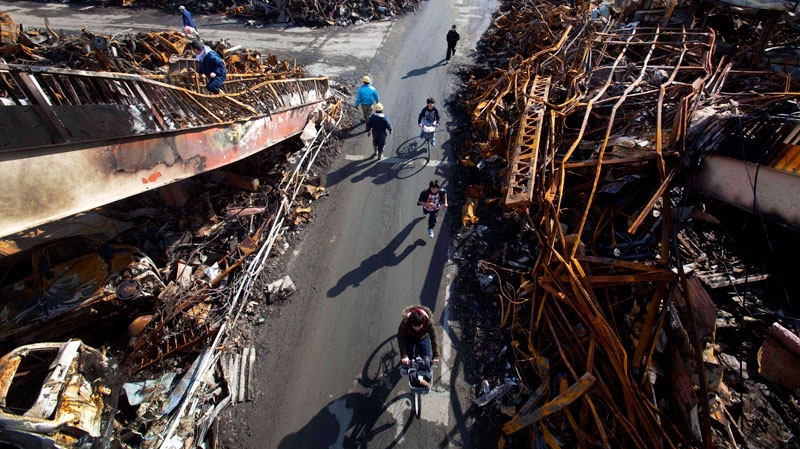 Japanese residents of Kesennuma, Japan, pass through a road that was cleared by bulldozer through the ruins of the city on March 17, 2011. (AP / David Guttenfelder)