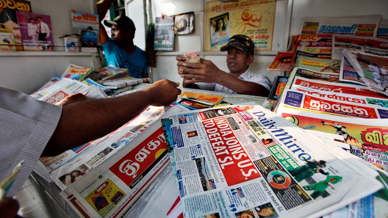 A newspaper vendor counts money as headlines refer to the resolution passed by the U.N Human Rights Council in Geneva, in Colombo, Sri Lanka, Friday, March 23, 2012. (AP / Gemunu Amarasinghe)