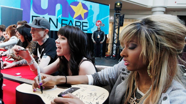 Musical artist Anjulie signs a guitar for a fan as Carley Rae Jepsen and Deadmau5 look on at the JUNO Fan Fare at a shopping mall in Ottawa, Saturday, March 31, 2012. (Fred Chartrand / THE CANADIAN PRESS)