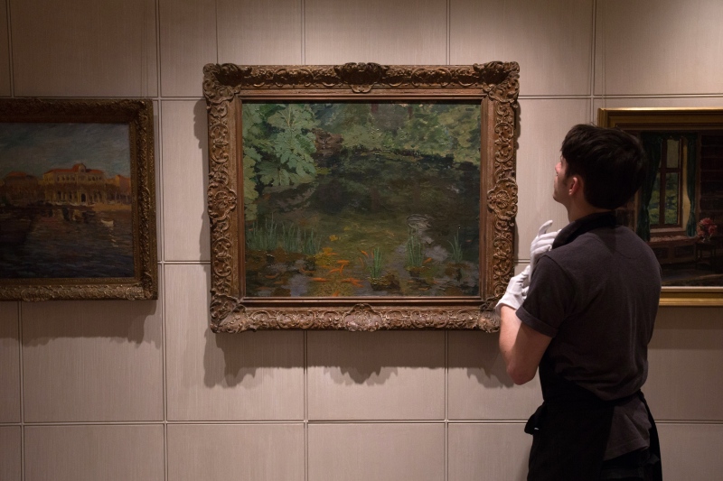 In this photo taken Tuesday, Dec. 9, 2014, a member of Sotheby's staff prepares to adjust a painting by Winston Churchill called 'The Goldfish Pool at Chartwell' at the auction house in London, England. (AP Photo/Tim Ireland)