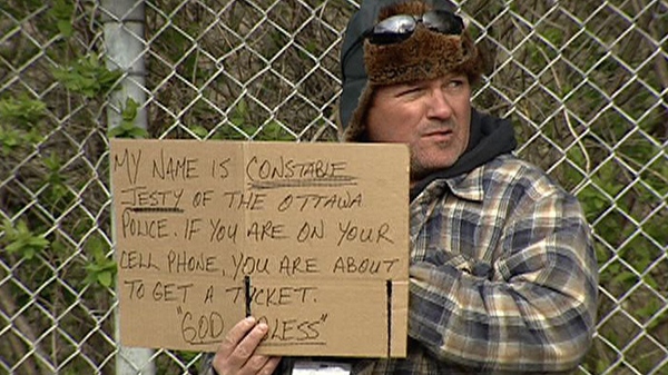 An Ottawa police officer holds a sign identifying himself as he tries to catch distracted drivers while posing as a panhandler Thursday, April 19, 2012
