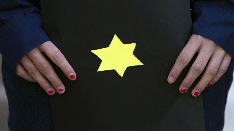 A girl holds a booklet with a yellow Star of David, symbolizing the sign identifying Jews during World War II, as Israeli activists hold a ceremony outside the German embassy in Tel Aviv, Israel on Holocaust Remembrance Day, Thursday, April 19, 2012. (AP Photo/Dan Balilty)