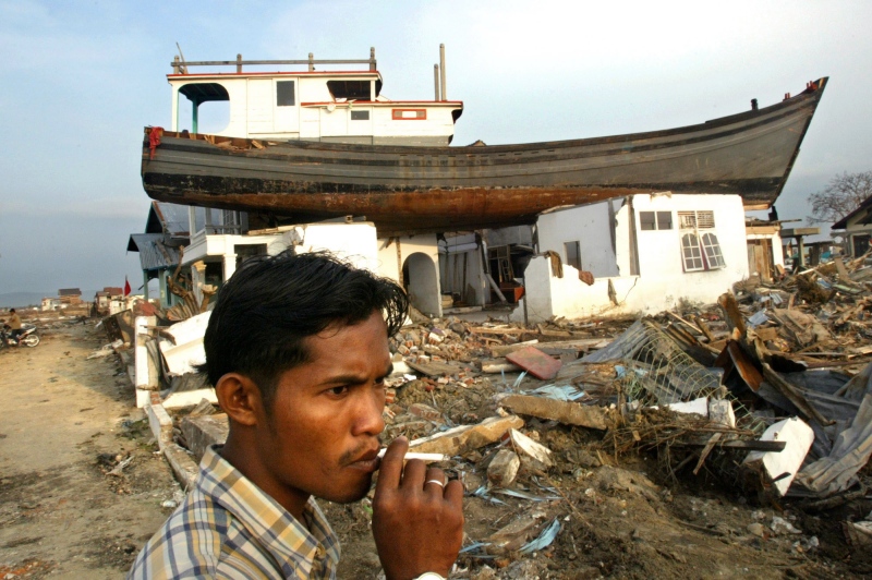 In this Feb. 17, 2005 file photo, an Acehnese man smokes a cigarette near a house on which a fishing boat landed after it was swept away by tsunami in Banda Aceh, Aceh province, Indonesia. (AP Photo/Dita Alangkara, File)