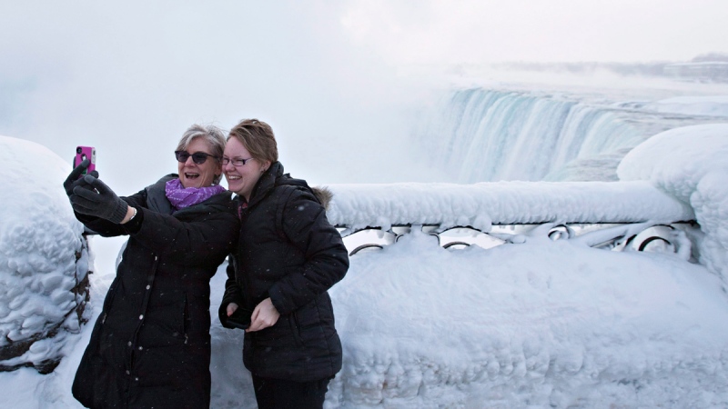 Visitors Rosalie Vissers, left, and Rachel Houter take a photo near masses of ice formed around the Canadian 'Horseshoe' Falls in Niagara Falls, Ont., February 19, 2015. (THE CANADIAN PRESS / Aaron Lynett)