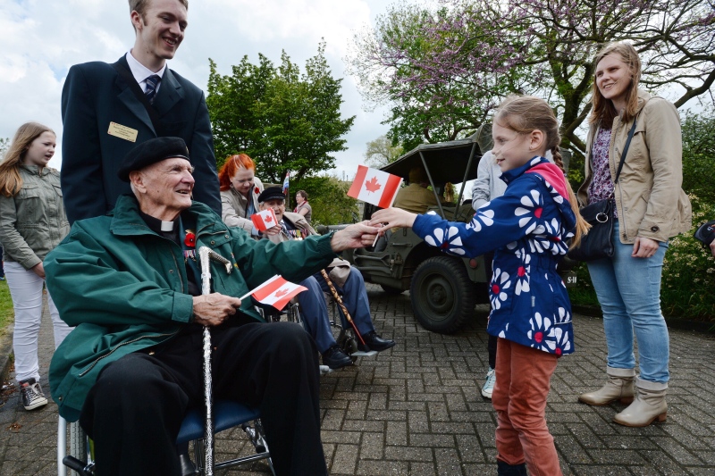 Canadian Second World War veteran Father R.S.H. Green, of Calgary, Alta., hands out Canadian flags to children during VE-Day celebrations in Wageningen, Netherlands, Tuesday, May 5, 2015. (Sean Kilpatrick / THE CANADIAN PRESS)