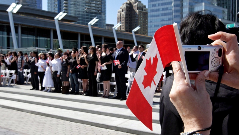 A woman takes a photograph while holding a Canadian flag as a group of 61 new Canadians take the oath of citizenship during a citizenship ceremony held as part of Canada Day celebrations in Vancouver, on Wednesday, July 1, 2009. (Darryl Dyck / THE CANADIAN PRESS)