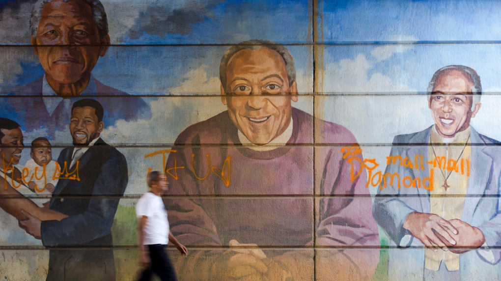 man walks past a mural depicting Bill Cosby