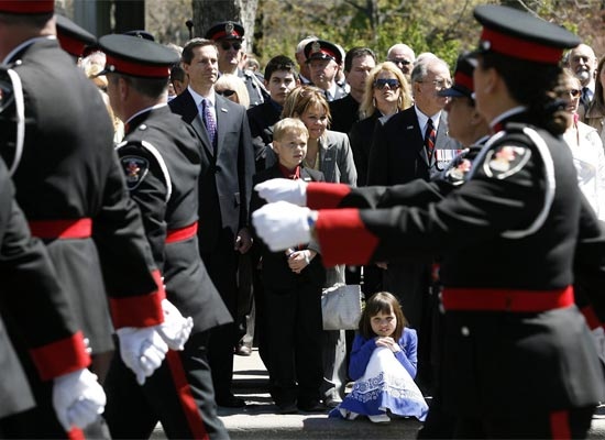 Const. John Atkinson's wife Shelley Atkinson, middle, smiles as she and her son Mitchell, 10, daughter Nicole, 8 and Ontario's Premier Dalton McGuinty watch thousands of police officers take part in honouring Ontario's fallen police officers on Sunday in Toronto (CP / Nathan Denette)