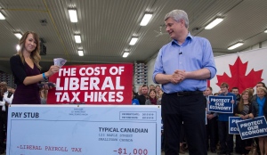 Conservative Leader Stephen Harper looks on as Nicole Ropp throws money on the counter as they illustrate how Liberal tax hikes will affect Canadians during a Conservative campaign event at an apple farm in Waterloo, Ont., Monday, Oct. 12, 2015. (Jonathan Hayward/THE CANADIAN PRESS)