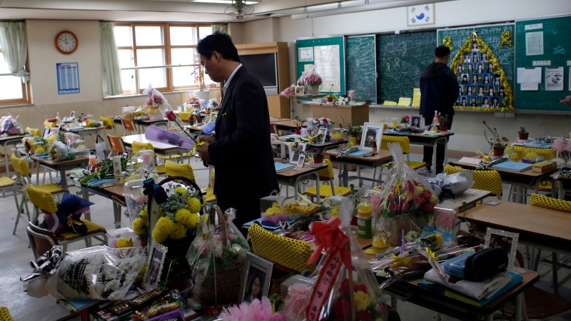People visit a classroom as flowers, notes and snacks from classmates and families paying tribute to the victims of the sinking of ferry Sewol are placed on the desks, at the Danwon High School in Ansan, South Korea, Saturday, April 16, 2016. (AP / Lee Jin-man)