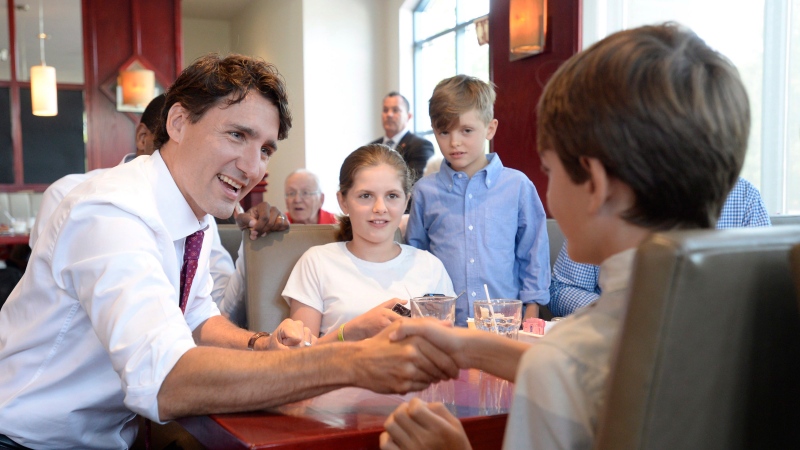 Prime Minister Justin Trudeau shakes hands with Russell Scarrow as Charlotte and James Faragher look on during a visit to a restaurant, in Aylmer, Que., Wednesday, July 20, 2016. (Adrian Wyld / THE CANADIAN PRESS)