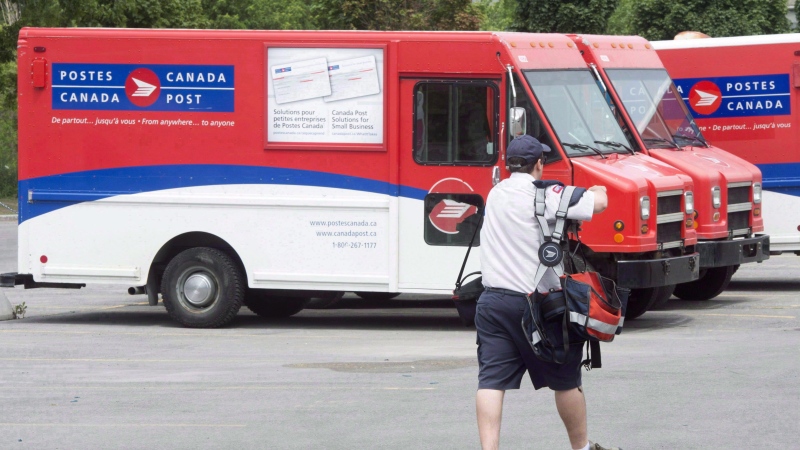 A postal worker walks past Canada Post trucks at a sorting centre in Montreal on July 8, 2016. (THE CANADIAN PRESS/Ryan Remiorz)