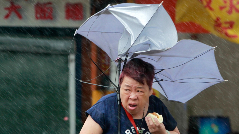 A woman eats and struggles with her umbrella
