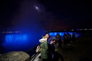 In this Saturday, Dec. 10, 2016 photo, people take a selfie near the Niagara Falls illuminated by new LED lights. (Julio Cortez / THE ASSOCIATED PRESS)