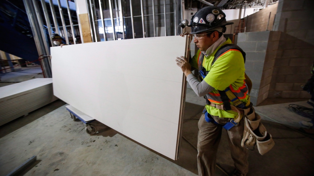 Construction workers move sheets of drywall